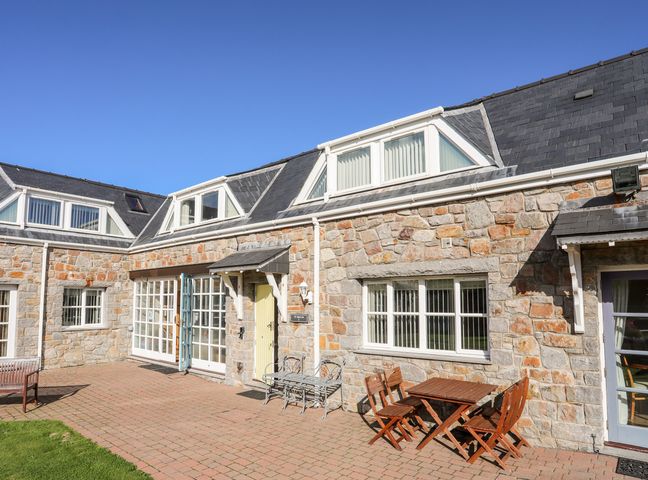 A stone exterior of a building with windows and doors and outdoor seating at Tyn Towyn - Ty Melyn in Trearddur Bay