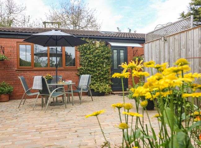 A patio with a table and four chairs under an umbrella in front of a brick house with a black door and climbing plants at Kilmory Lodge in Stalmine near Poulton-le-Fylde