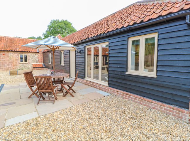 An outdoor patio with a wooden table and chairs under a striped umbrella at The Granary Willow Grange Barns Stanfield