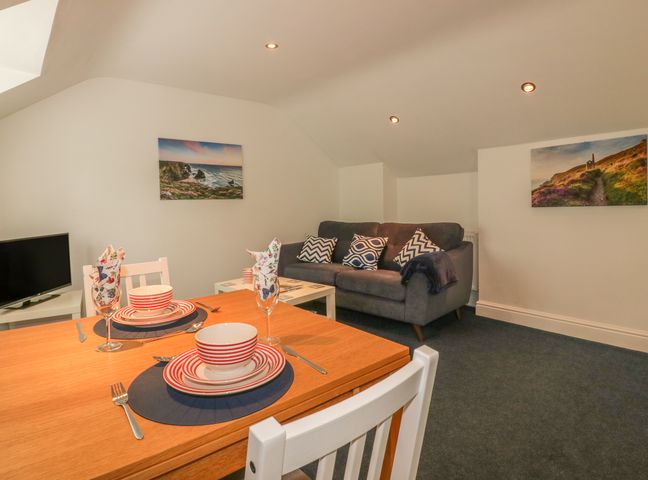 A dining table set with plates bowls glasses and cutlery next to a sitting area with a sofa and cushions in Summer Breezes Crantock