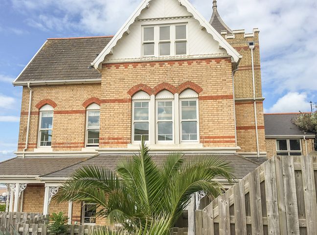 A brick house with arched windows and a wooden fence with a palm tree in front at Seashore in Woolacombe