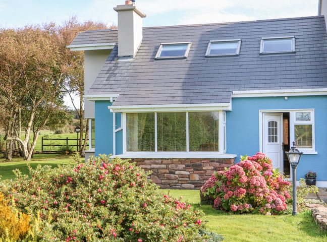 A garden with bushes and flowers in front of a blue house with windows and a door at The Blue Annex The Spa near Tralee County Kerry