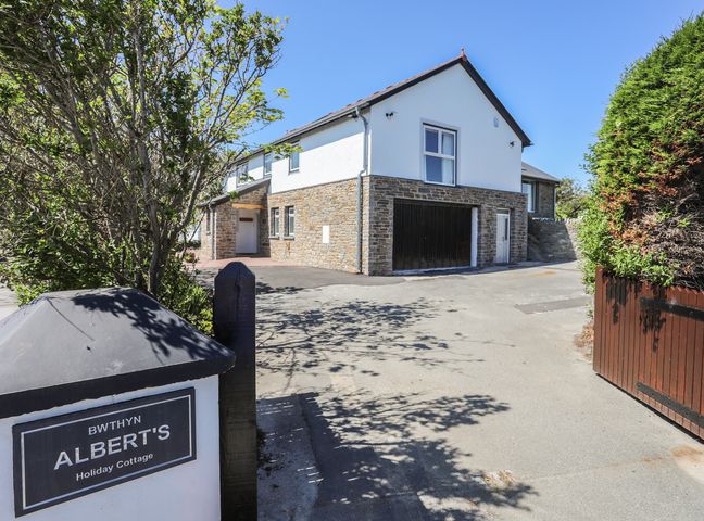 Entrance view of a two story holiday cottage with stone and white walls and driveway at Bwthyn Alberts in Trearddur Bay