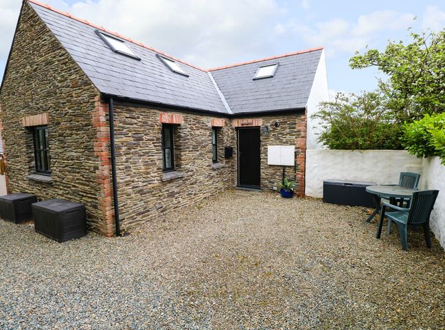 A courtyard with stone building walls and slate roof with windows and a door with plastic chairs and table at The Old Stables in Fishguard