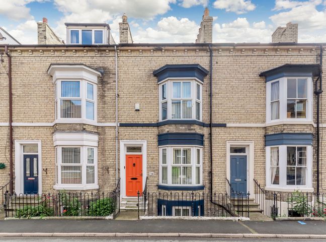 A row of brick townhouses with bay windows and colored doors on a street at Salty Fox in Whitby