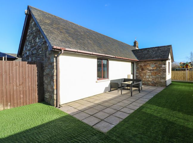 An outdoor patio area with tiled floor artificial grass seating and stone and white walls at The Old Well Bungalow - Ty Mawr Farm in Cardiff