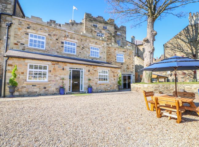 An outdoor courtyard with a gravel surface wooden picnic table with umbrella and a stone building with windows and doors at Castle keep at Stanhope Castle in Stanhope