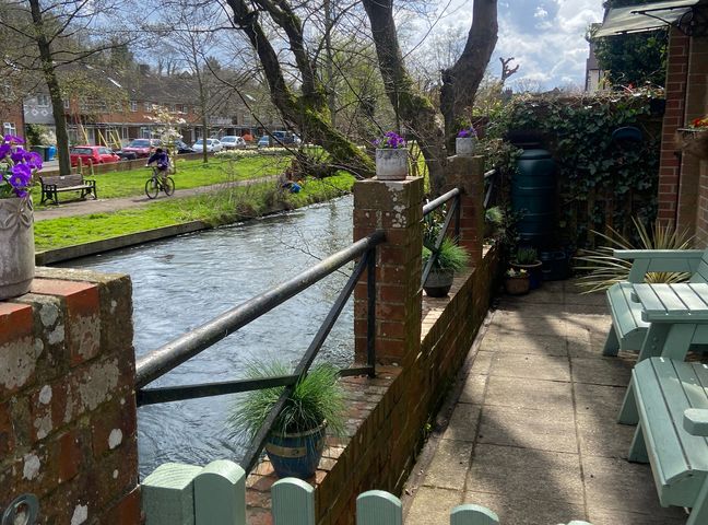 A riverside patio with potted plants and green wooden chairs next to a brick wall and railing at RiverGem - Riverside Coach House in Winchester