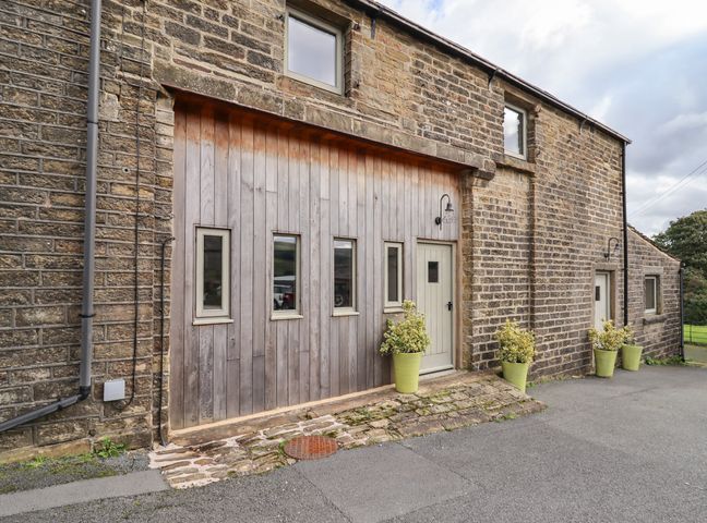 Exterior of a stone building with wooden panels small windows doors and potted plants at The Cow Shed in Holme Yorkshire