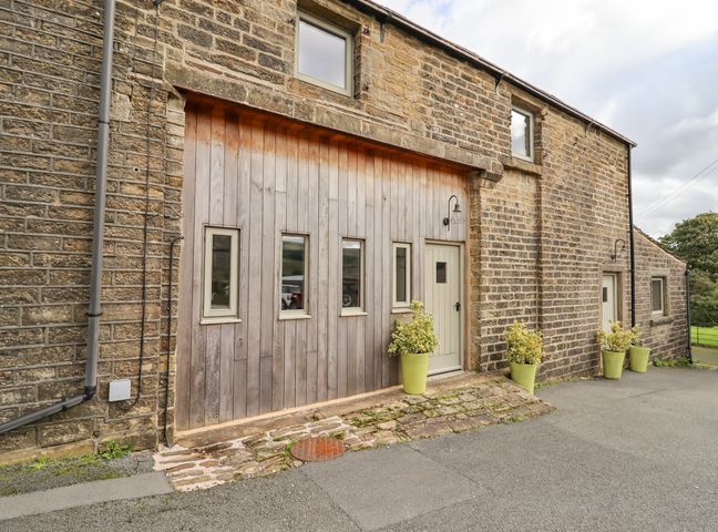 The exterior of a stone building with wooden doors and small windows and plants in pots outside at The Hayloft in Holme Yorkshire