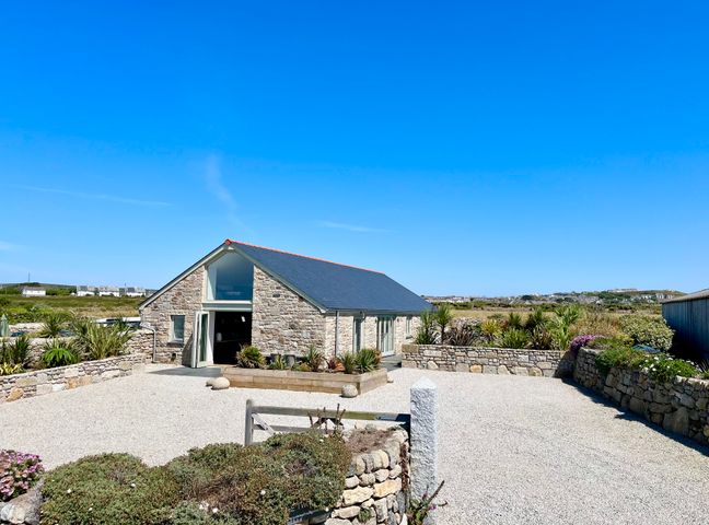 A stone building with a slate roof and gravel courtyard surrounded by stone walls and plants at See Two Seas Cape Cornwall in St Just
