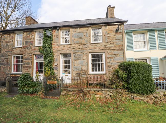 Stone exterior of a terraced house with white framed windows and doors small garden with bushes and a wooden bench at Brackenbury Cottage in Beddgelert