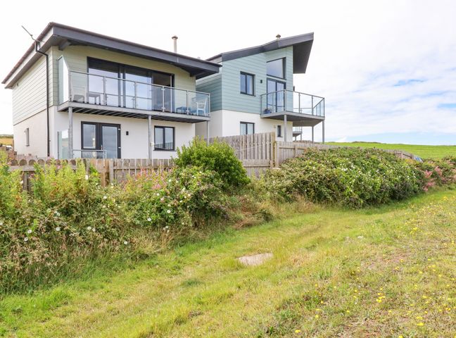 A modern two-story house with balconies wooden fence and green bushes in a grassy area at Sandpiper in Perranporth