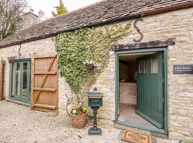 Stone exterior of a barn with a green stable door open a wooden shutter and climbing ivy at Five Mile House Barn in Duntisbourne Abbots near Cirencester