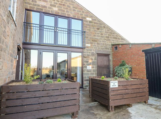 An outdoor area with two large wooden planters in front of a stone building with glass doors at The Hayloft in Spofforth