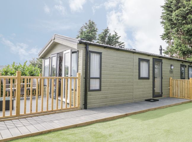 A small house with a wooden deck and railing surrounded by trees at The Maple in Cloughton