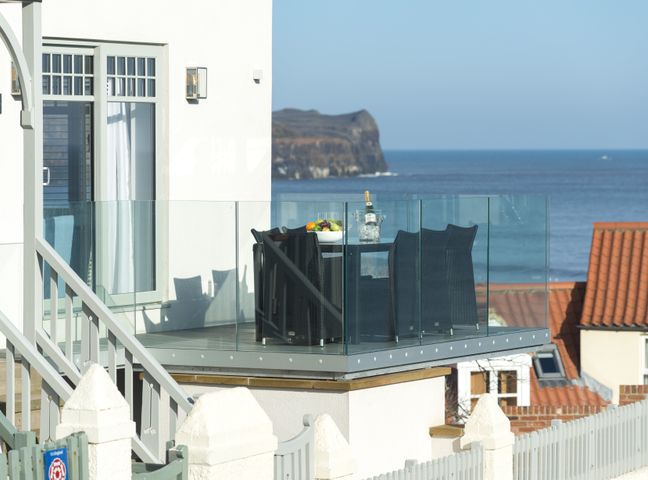 A balcony with a glass railing and a table with chairs overlooking the sea at Shore View in Sandsend