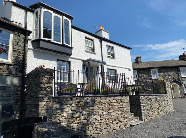 A white house with stone walls and a black iron fence around a patio with chairs and plants at Prospect House in Ambleside