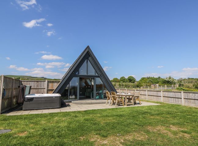 An outdoor patio with a hot tub and wooden table with chairs next to an a frame building at Elan Valley Welsh - The Sheepfold in Llanyre near Llandrindod Wells
