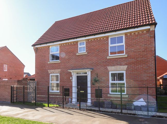 A brick house with a tiled roof a black door and several windows behind a black metal fence at Derwent House in Pickering