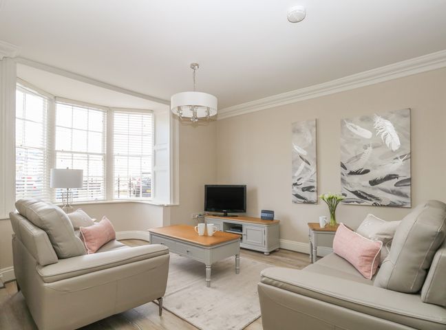 A living room with two sofas a coffee table a TV and paintings on the wall at Harbour Watch 2 in Weymouth