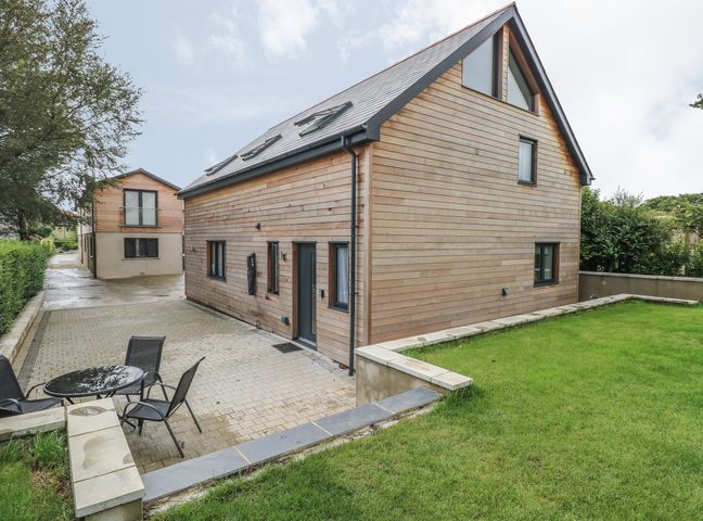 A wooden house with a small patio area with table and chairs and a green lawn at The Boathouse in Tenby