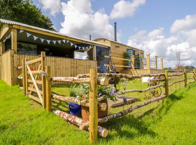 A wooden cabin with a fenced garden and a seating area at High Rigg Shepherd's Retreat in Brampton Cumbria