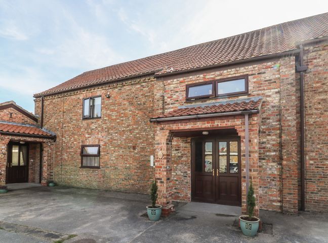 A brick building with double wooden doors and two potted plants outside at Thistle in Barlby