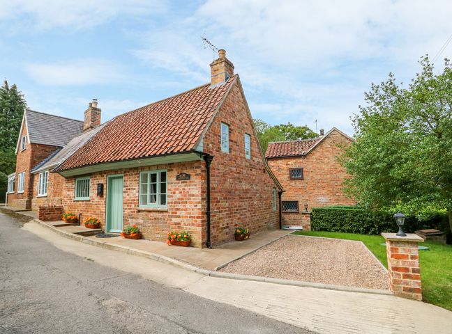 A brick cottage with a tiled roof and green door next to a gravel driveway and trees at Lizzies Cottage in Horncastle