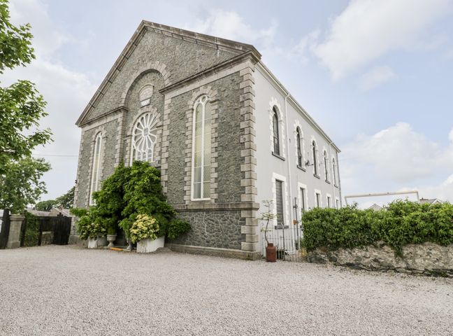 An exterior view of a stone and white building with arched windows and greenery at Capel Mawr Basement 19 Llanrug