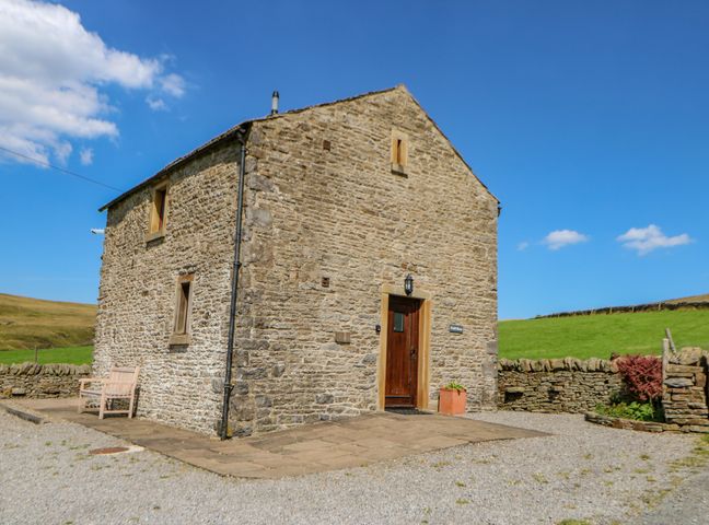 A stone house with wooden door and bench outside in a rural area at Field Barn in Alston