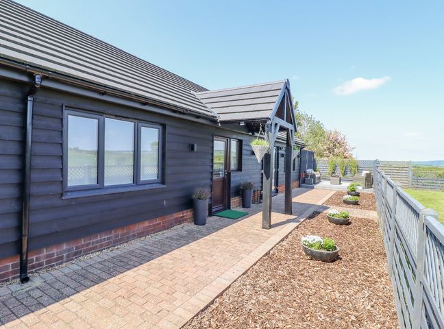 An outdoor pathway with flower pots leading to the entrance of a black wooden house at Closefield in Ivinghoe Aston near Ivinghoe