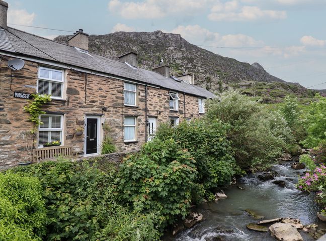 Stone terraced houses with a bench and a flowing stream beside vegetation at 3 Barlwyd Terrace in Tanygrisiau near Blaenau Ffestiniog