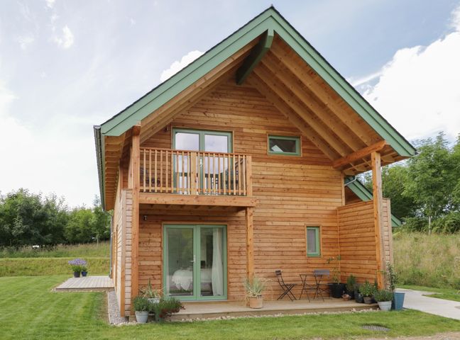 A wooden house with a balcony and patio furniture surrounded by grass at Na Clamhanan Rafford near Forres