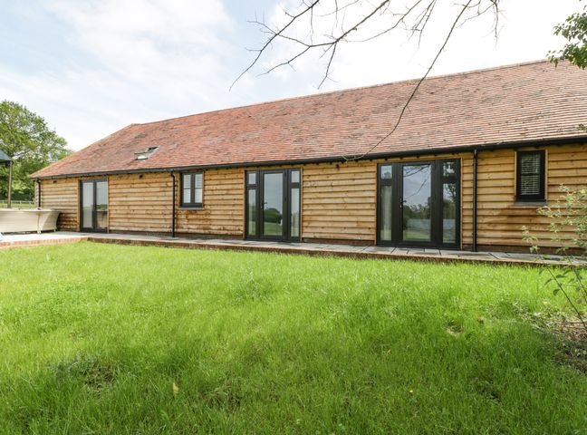 A wooden house with multiple black framed windows and glass doors facing a green lawn at The Old Dairy in Finchampstead