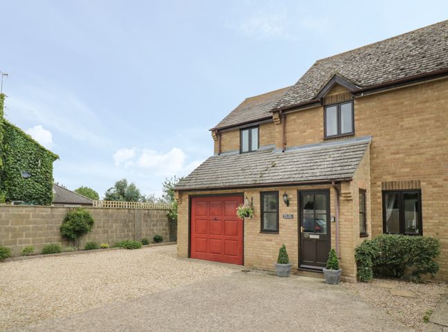 A brick house with a red garage door and a brown entrance door with plants in pots at Kite Cottage in Syresham