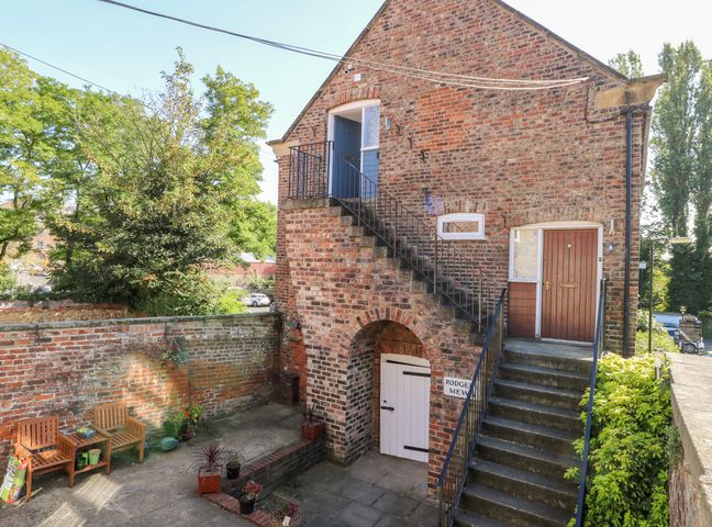 A brick building with exterior stairs leading to a door a courtyard with chairs and potted plants at 2 Rodgers Mews in Malton