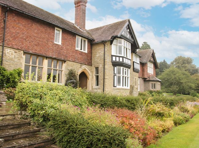 A stone and brick house with multiple windows surrounded by shrubs and a garden at The Old Nursery in Bourton near Much Wenlock