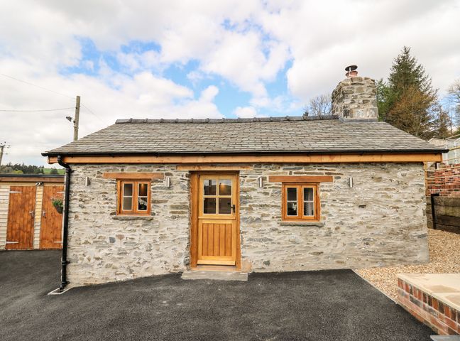 Stone cottage with wooden door and windows and a chimney in a rural setting at The Old Cobblers Shop in Llanbister near Llandrindod Wells