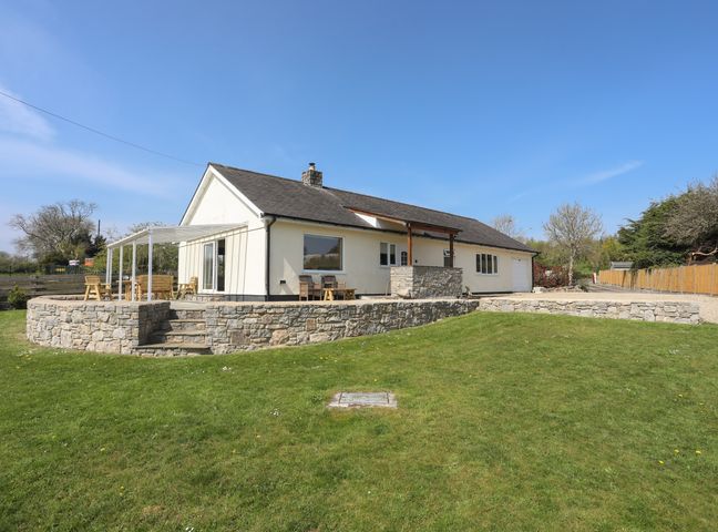 A bungalow with a stone terrace and lawn in a rural setting at Cae Capel in Pentraeth