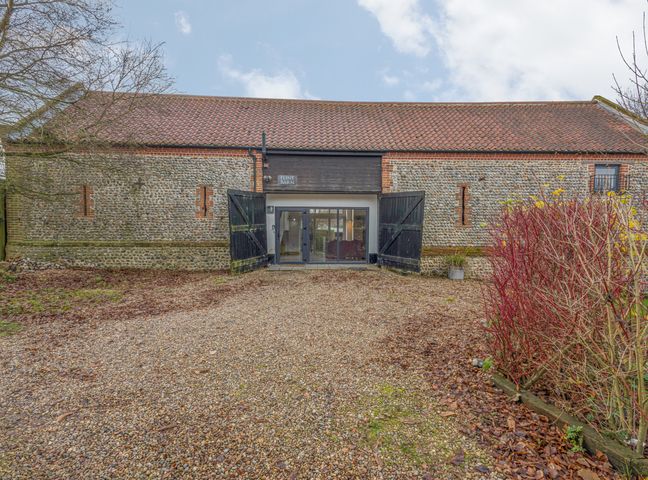 The exterior of a stone and brick barn with open black wooden doors and gravel driveway at Flint Barn in Knapton
