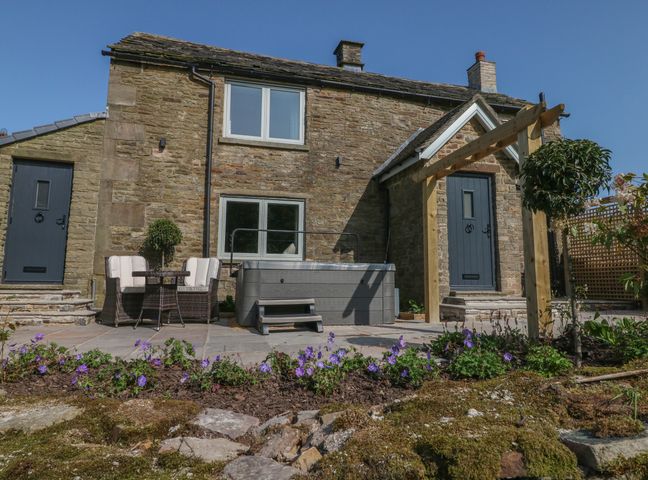 A stone house with blue doors and a patio with outdoor chairs a hot tub and flowers at Overlea Cottage in Hayfield