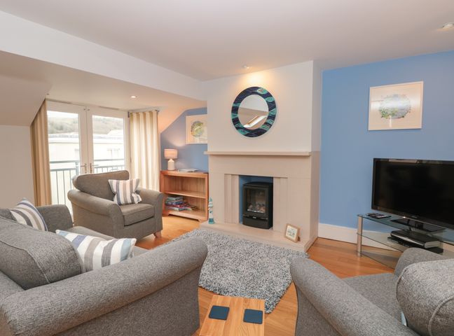 A living room with grey armchairs and sofa a fireplace and a television at 42 Dart Marina Dartmouth