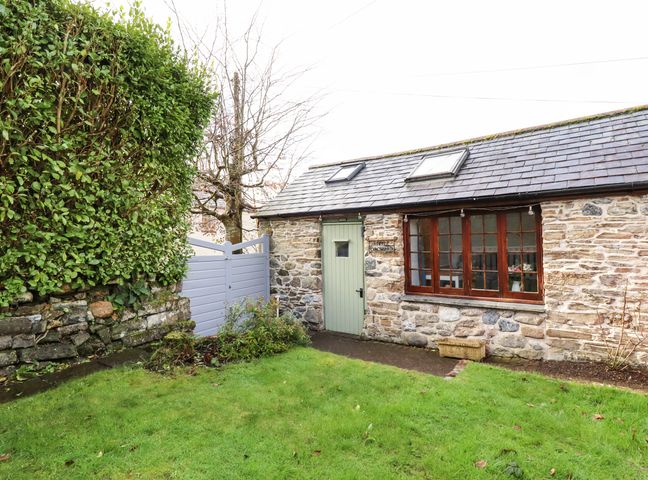 A stone cottage with a green door and wooden windows in a garden with grass and a hedge at Little Orchard Barn in St Austell