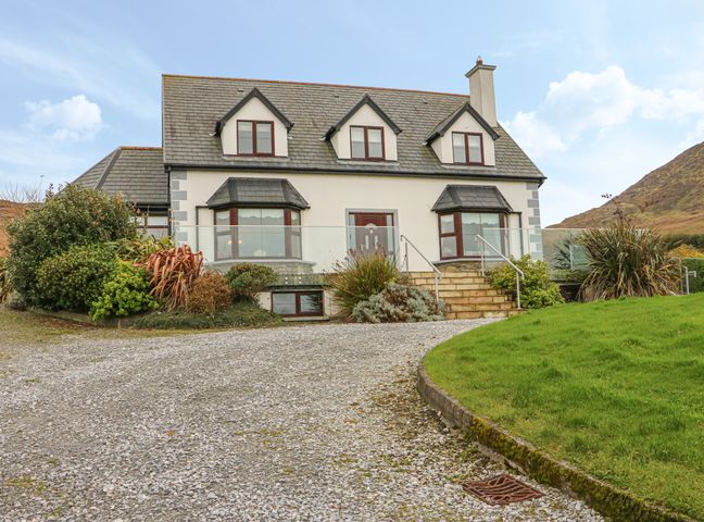 A two-story house with dormer windows a gravel driveway and shrubs at Starbay House in Eyeries County Cork