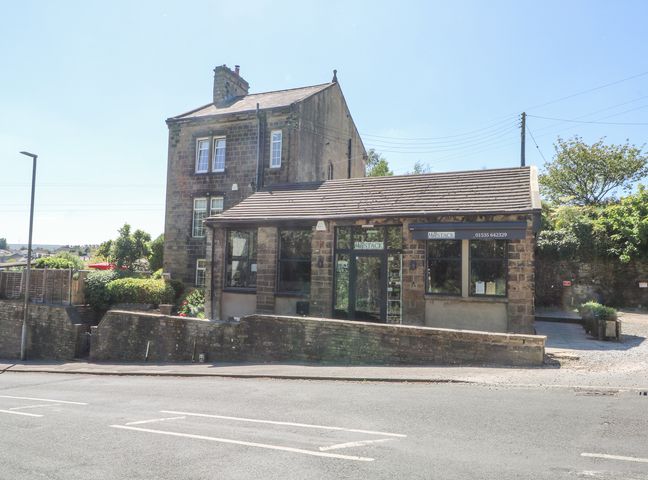 A stone building with a small single-story extension and a paved area outside at The Stone Masons House in Oakworth