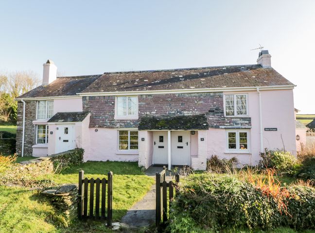 A pink stone cottage with two white doors and a garden gate at 2 Rose Cottages Lansallos near Polperro