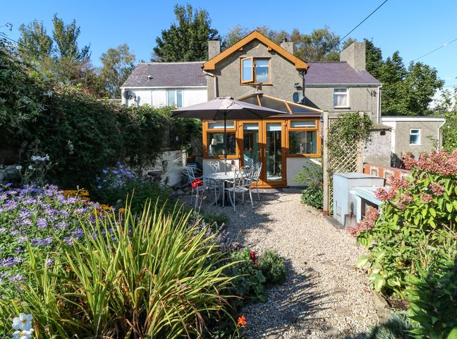 A garden with plants and flowers and a patio table with an umbrella outside a house at Bwthyn Y Felin in Y Ffor near Pwllheli