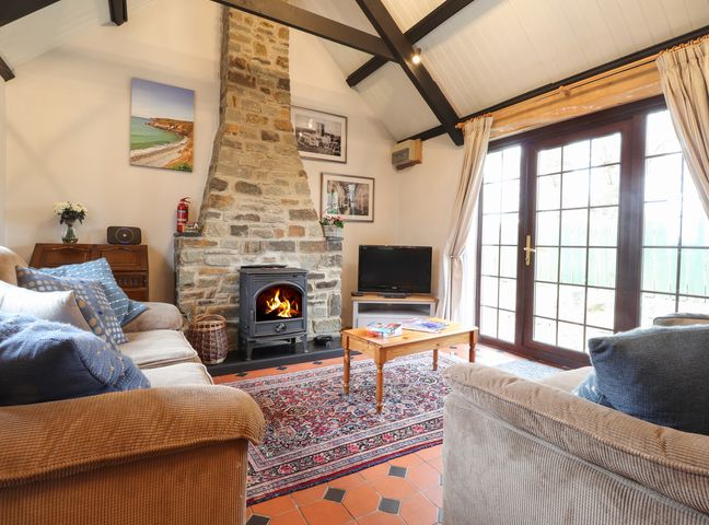 A living room with two sofas a stone fireplace and a TV next to glass doors at Bwthyn Alarch in Trefin St Davids Pembrokeshire