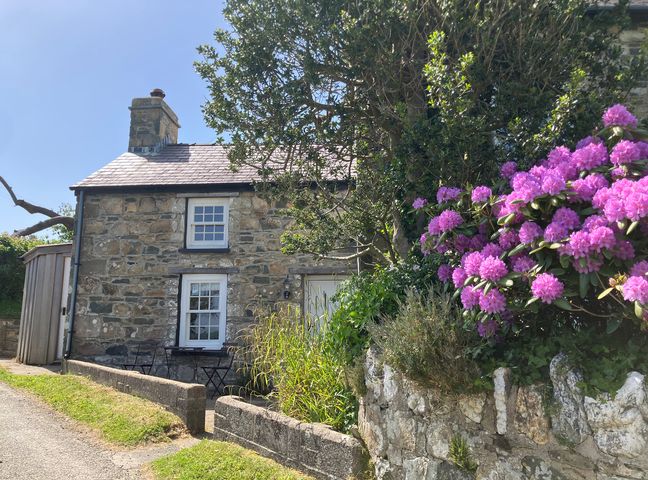 A stone cottage with flowers and chairs outside at West End Cottage in Newport, Pembrokeshire